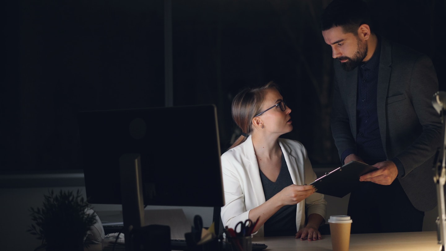 Professionisti aziendali che discutono documenti a una scrivania a tarda notte.
