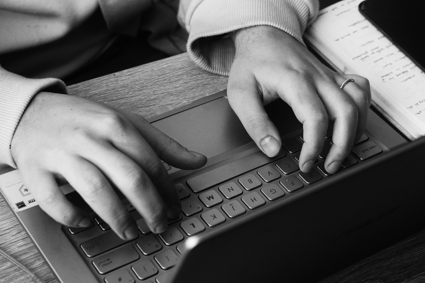 Mani che digitano su una tastiera di un laptop argentato su una scrivania di legno.